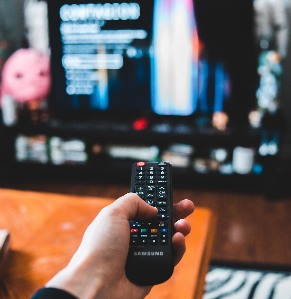 Hand holding TV remote control in front of an out of focus TV