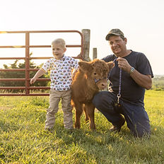 Highland cow meet and greet with a young child and man smiling beside a Highland calf.