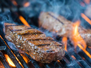 a sizzling steak on the grill with flames licking the edges