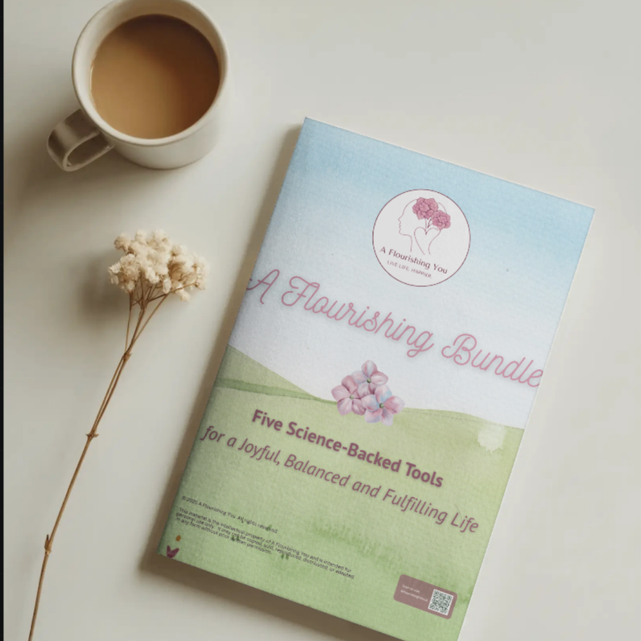 Flat lay of A Flourishing Bundle positive psychology workbook on a clean desk beside a coffee cup and dried flower.