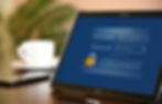Tablet with login screen displaying username, password fields, and login/register buttons. Blurred coffee cup and phone in background.