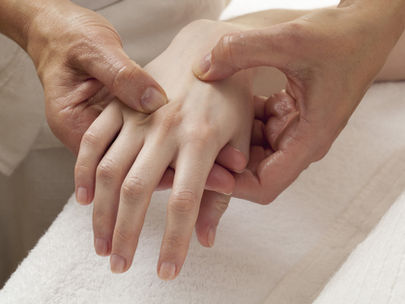 Hands performing a gentle hand massage on a white towel. The skin tones contrast with the soft, neutral background, conveying relaxation.