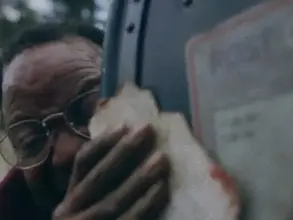 A man holds a blood-stained piece of paper against a mail box