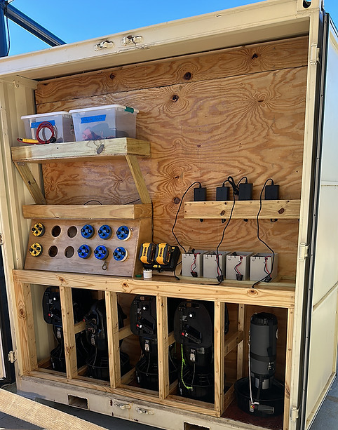 "Custom wooden storage and charging station for underwater scooters inside a plywood-lined enclosure: upper shelves hold plas