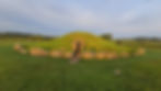 Bryn Celli Ddu tomb in Anglesey illuminated by morning sunlight, with the photographer’s shadow cast on the grass-covered mound during solstice.