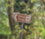 Roadside heritage sign pointing toward Belas Knap Long Barrow near Winchcombe, marking the approach to the Neolithic Cotswold–Severn chambered tomb in Gloucestershire.