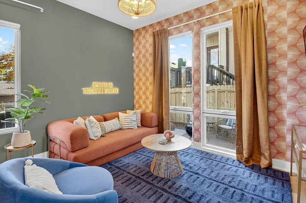 Modern living room with burnt orange sofa, blue accent chair, and neon Tennessee Whiskey sign, perfect for group dining