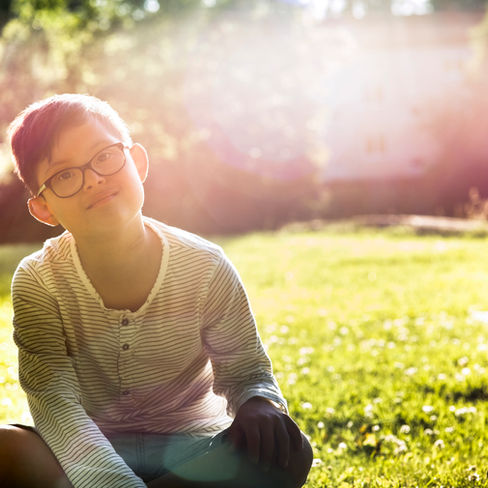 boy with glasses sitting on a sun-drenched lawn