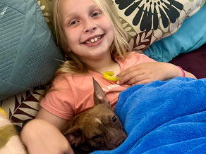 female child on couch with puppy beside her