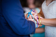 Close up picture of bride and groom's hands tied with colorful blue, purple and yellow rib