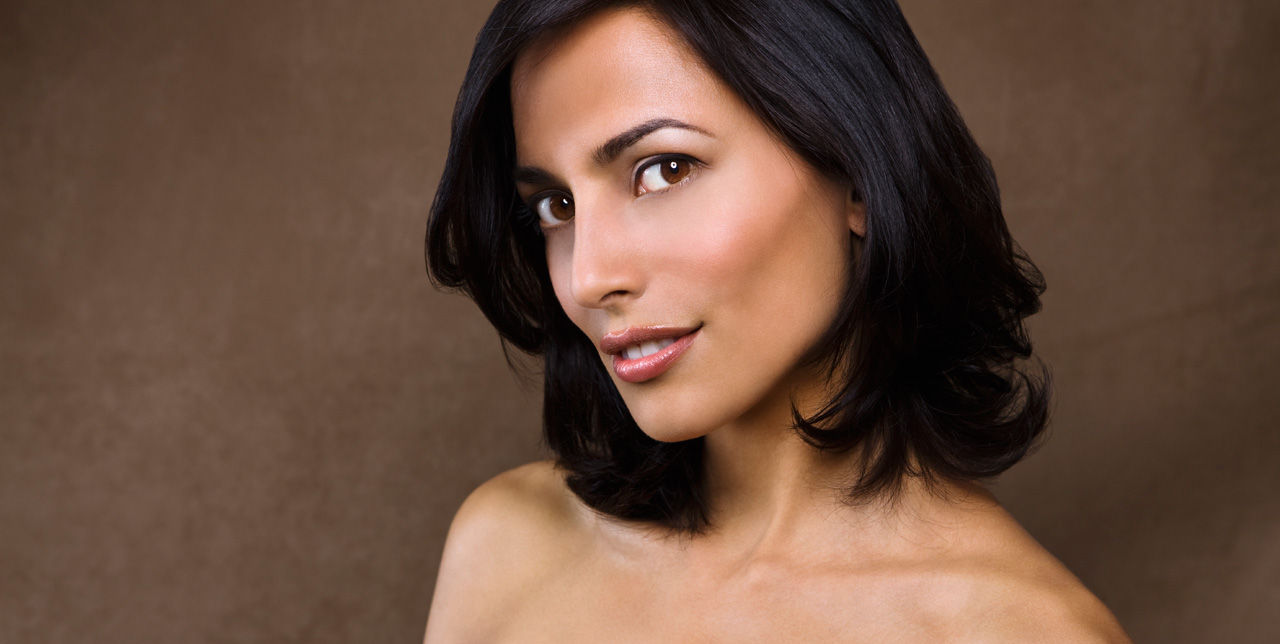 A dark haired woman glances sideways at the camera, her shoulders exposed.