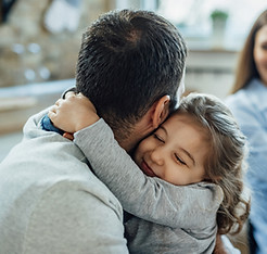 affectionate-little-girl-with-eyes-closed-embracing-her-father-home-mother-is-background.j