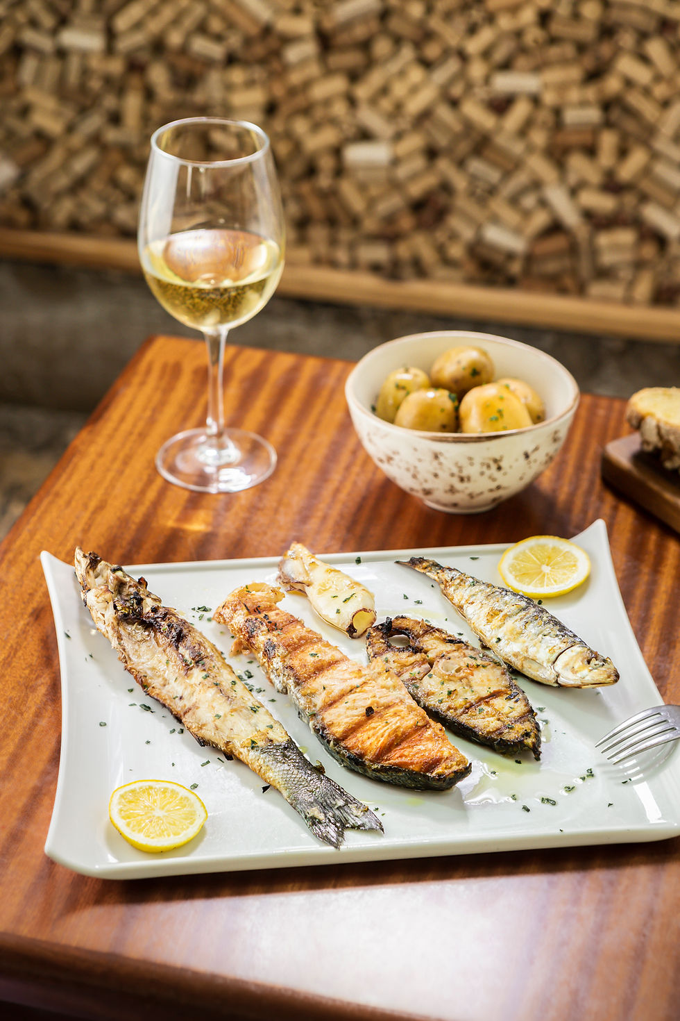 prato de peixes grelhados com fatia de limão acompanhado por copo de vinho branco