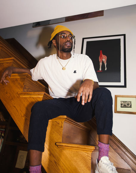 d.p.thuH wearing a yellow beanie and white shirt, seated on wooden steps