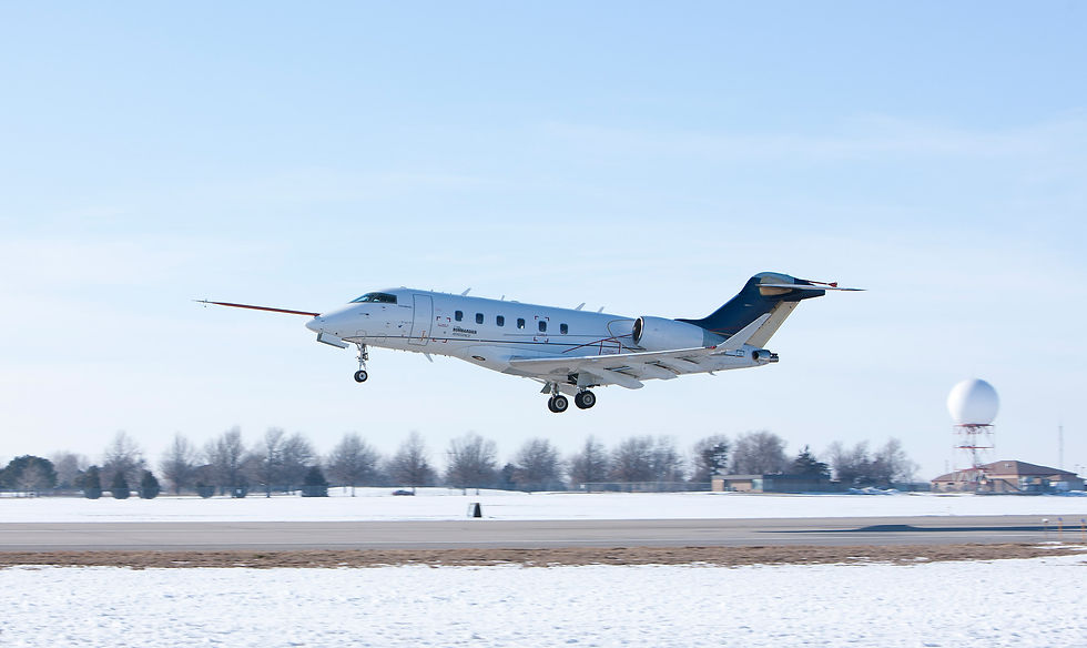 Bombardier Challenger 350 jet landing over a snowy runway under a clear blue sky