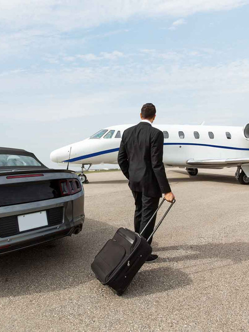 businessman walking with suitcase from car to private jet
