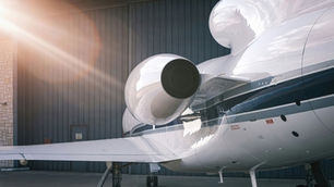 Close-up of a white private jet's engine with blue stripes, parked outside a hangar.