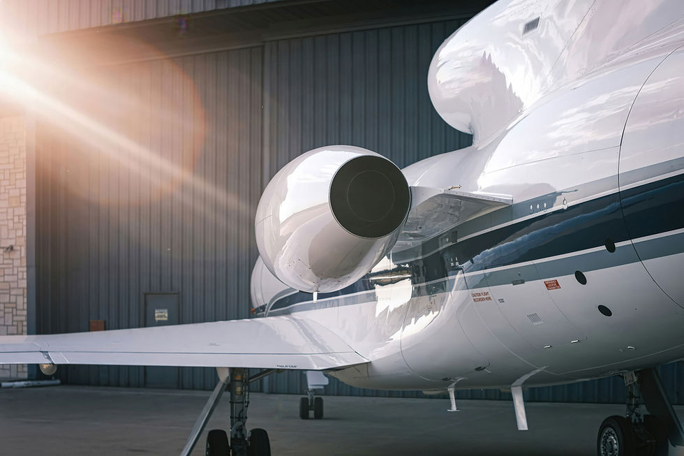 Close-up of a white private jet's engine with blue stripes, parked outside a hangar. 