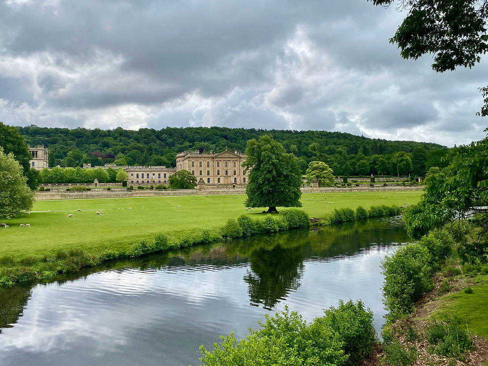 A cloudy morning looking at Chatsworth House in England, with a creek in front of it and sheep on the lawn