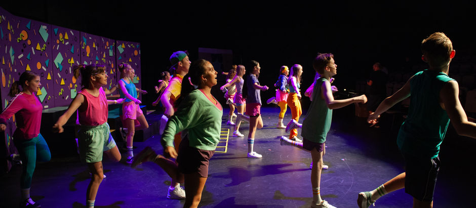 West Jordan Youth Theater cast performing in their recent production of Freaky Friday, with young actors in colorful costumes dancing energetically on stage under bright theater lights.
