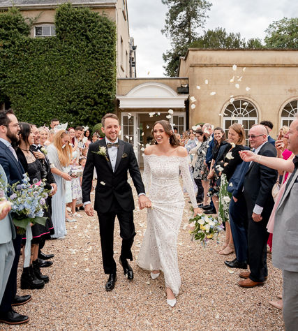 A couple walk through white confetti at Northbrook Park