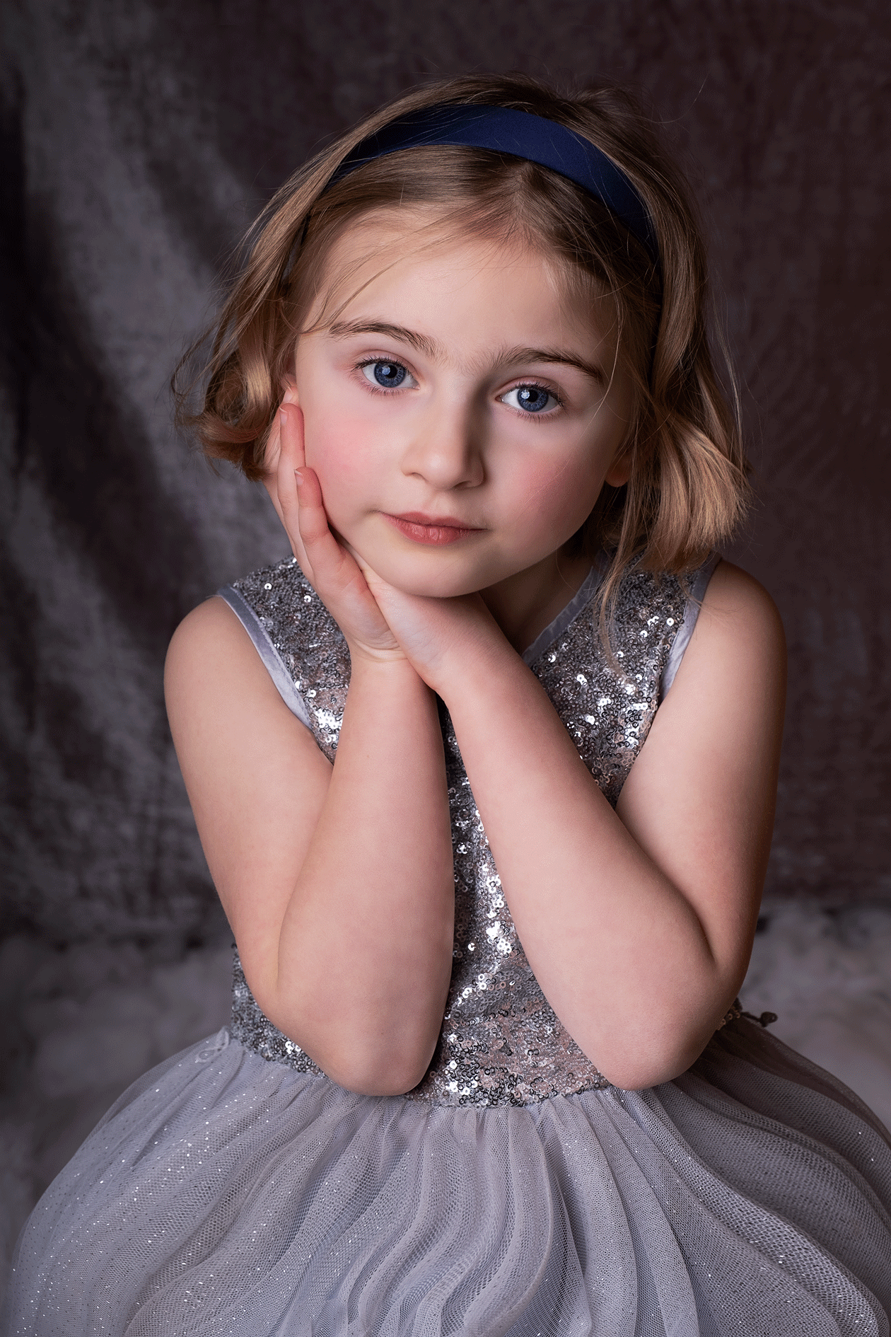 a little blonde girl holds her hands beside her face, silver dress 