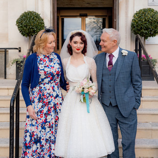 A vintage bride stood in between her parents on the the steps of Islington Town Hall