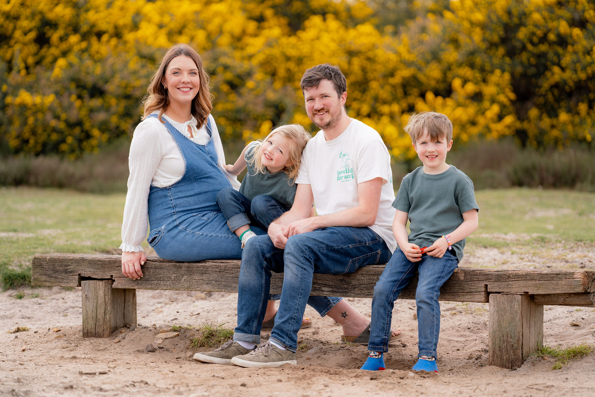 A family with a pregnant mum in denim overalls on a bench at Frensham Little Pond