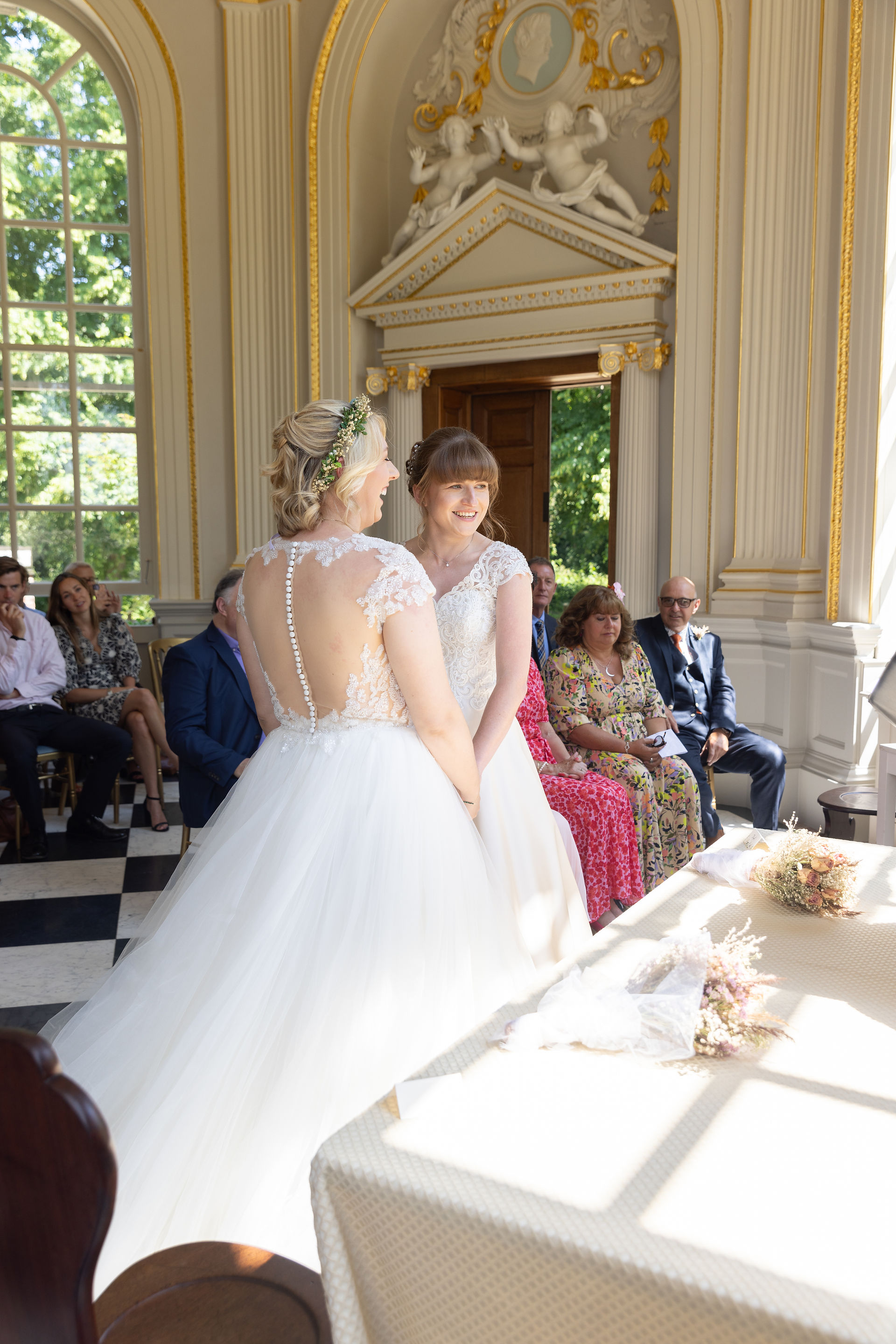 Brides face each other and smile as they commit to each other in a wedding ceremony 