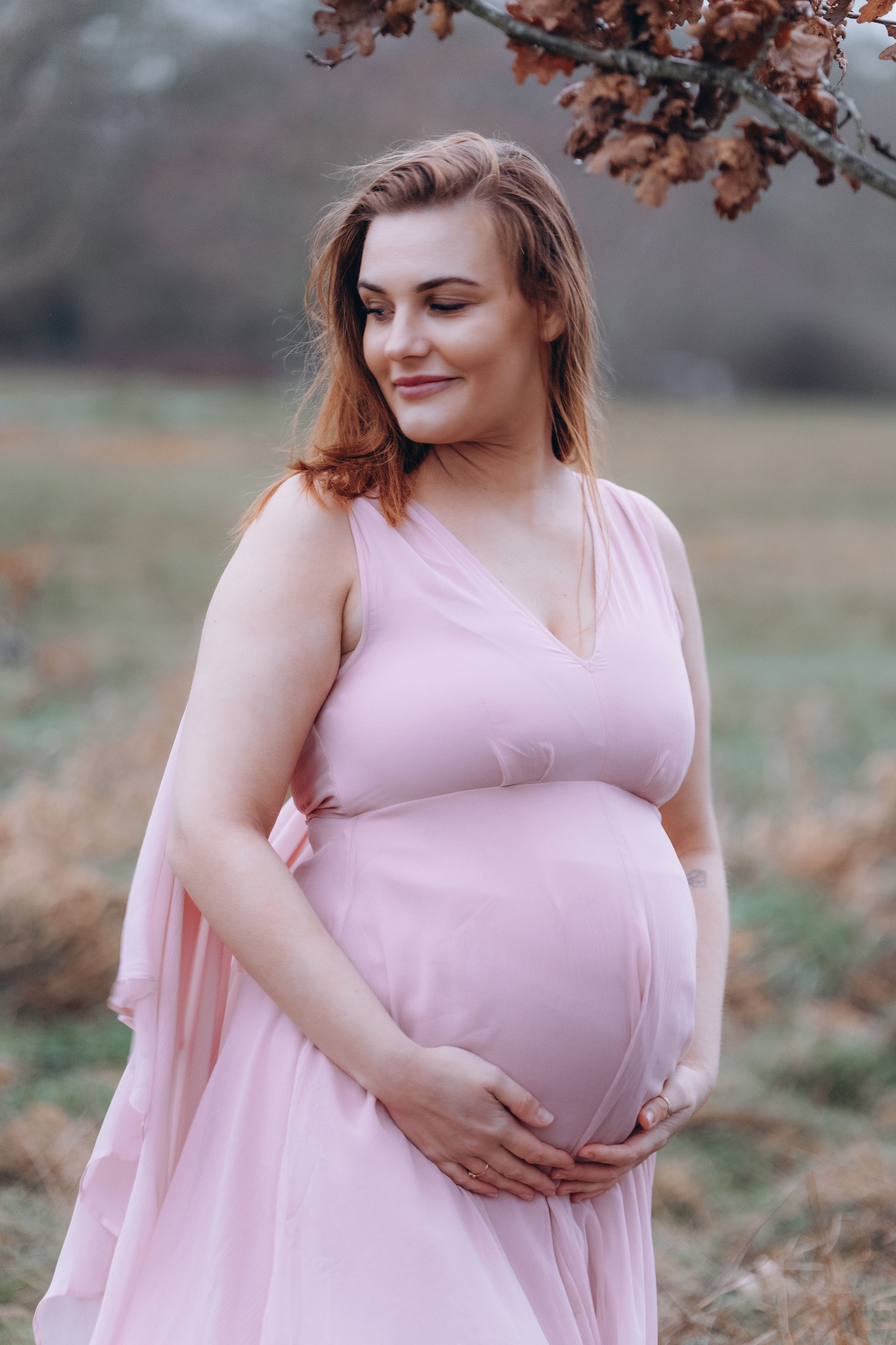 A red-haired woman stands clutching her pregnant belly in a field in Farnham Surrey 