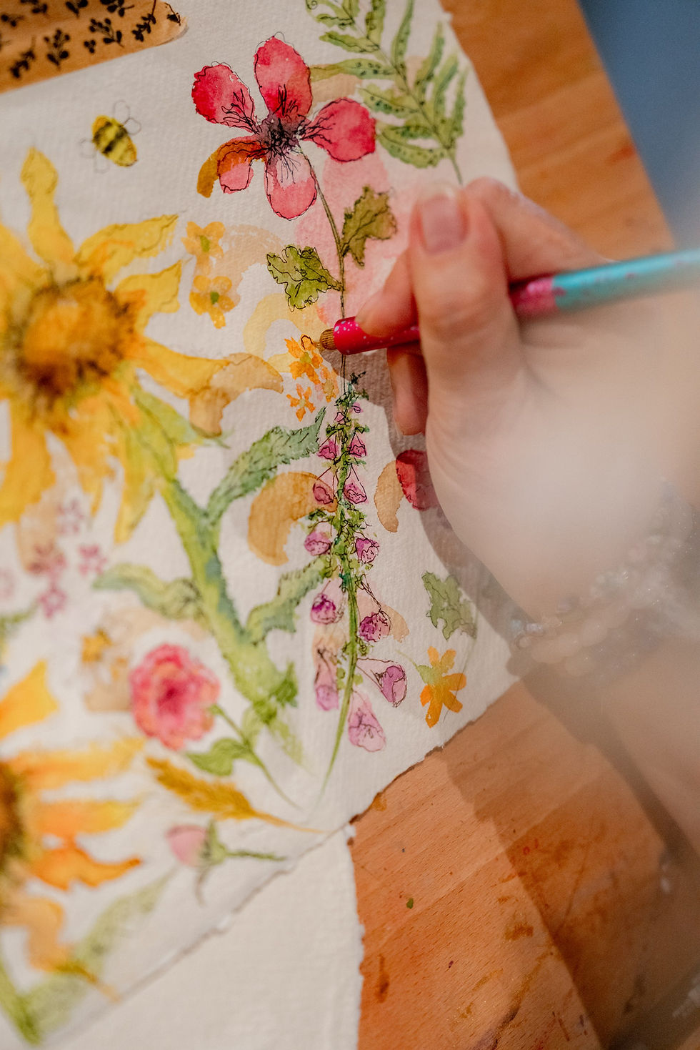 A womans hand draws on a watercolour painting of flowers