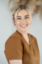 Smiling person in a brown top against a neutral background, exuding a cheerful and welcoming vibe.