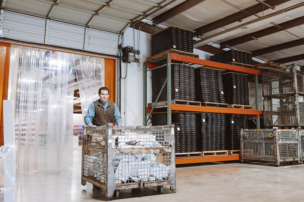 Man pushing a metal cart inside the warehouse with stacked shelves and supplies.