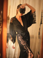 Woman wearing a long black silk robe with lace insets tied up at the leg. 