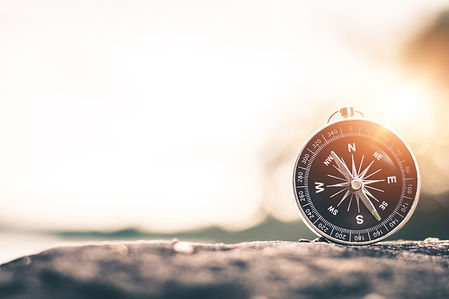 A compass pointing near North sits on a rock with a sunset in the background