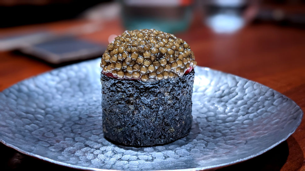 Cylindrical charcoal-hued creation topped with glistening caviar, plated on a textured gray dish at JUA.
