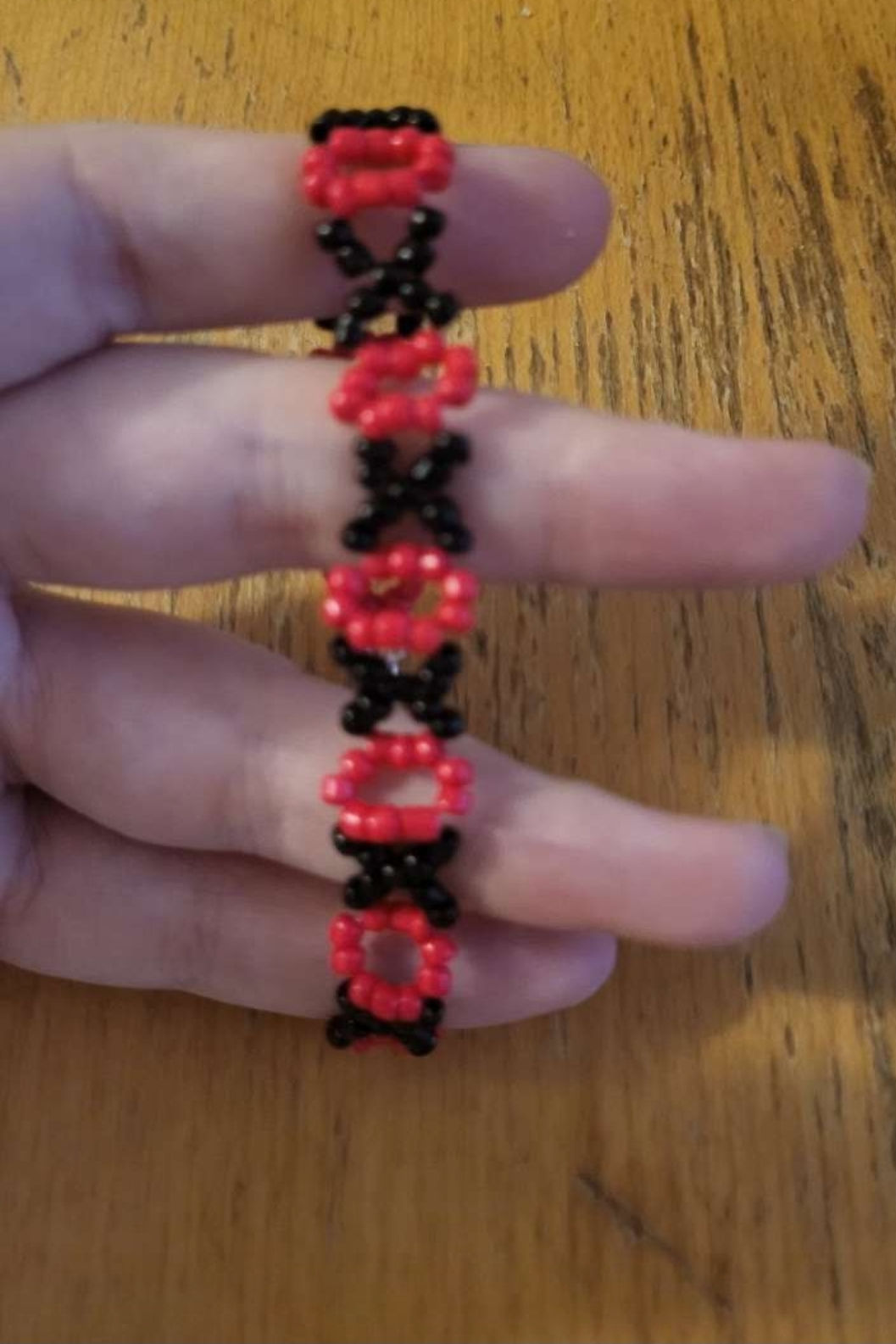 Bracelet rouge et noir sur une main. Kissbijoux, Classique, sur fond bois.