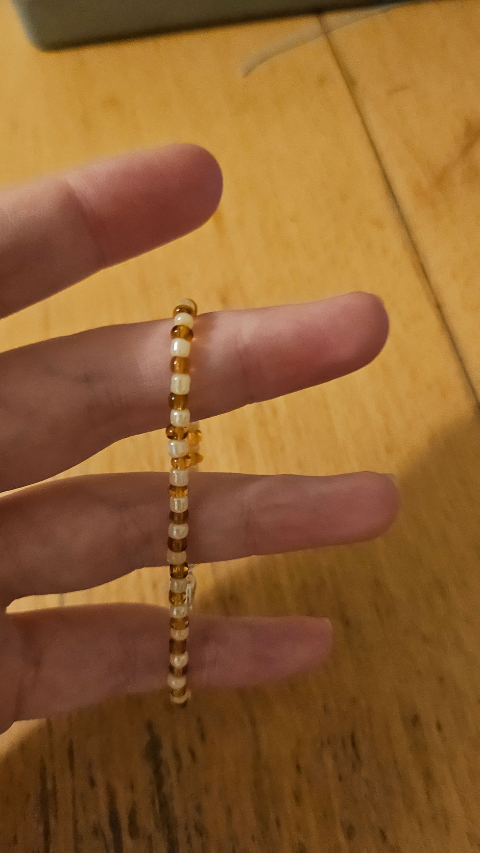Bracelet de perles blanches et ambrées porté sur un doigt, Kissbijoux, près.