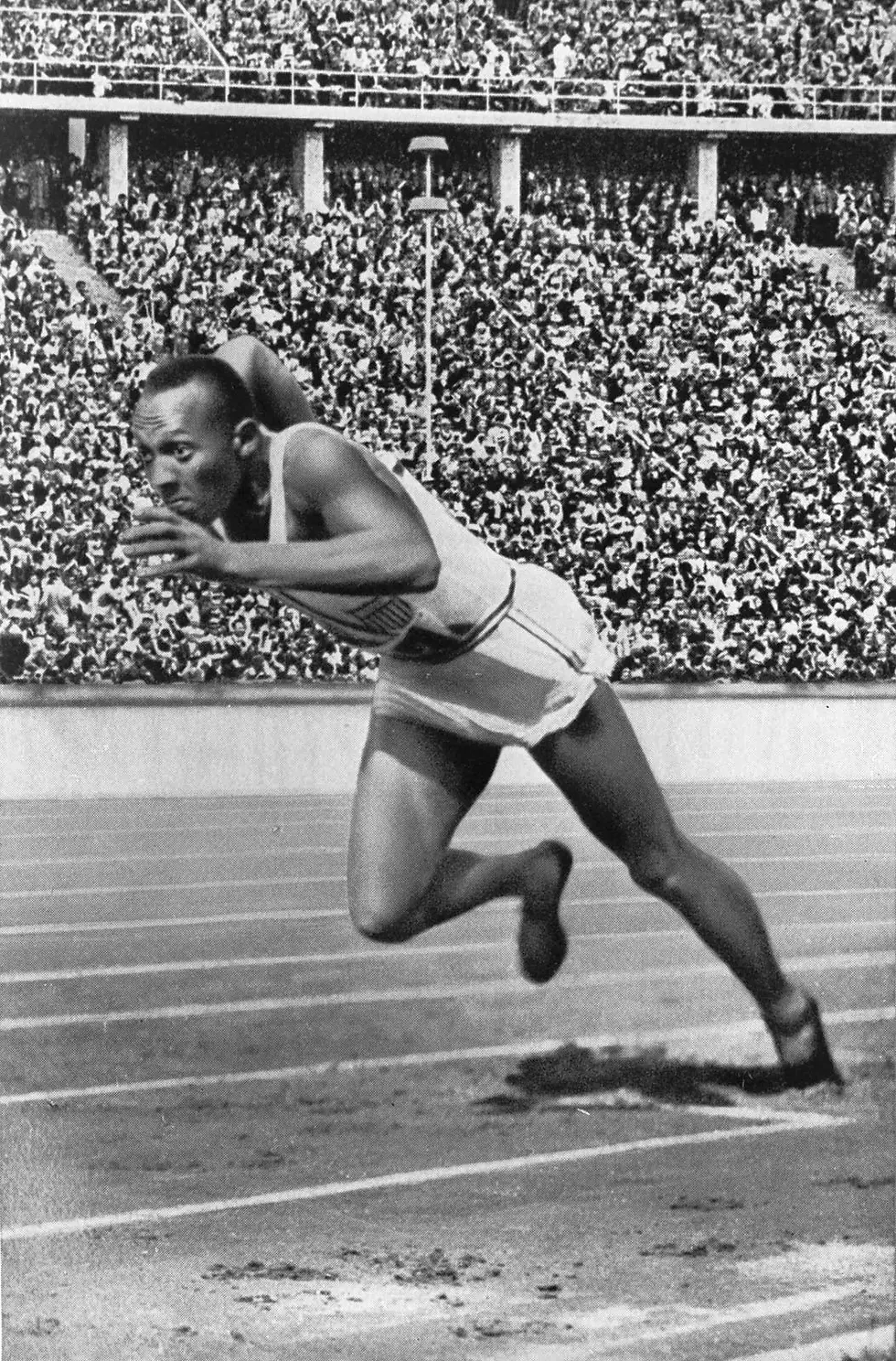 Man starting to run the 100 meter dash with crowd cheering behind him.