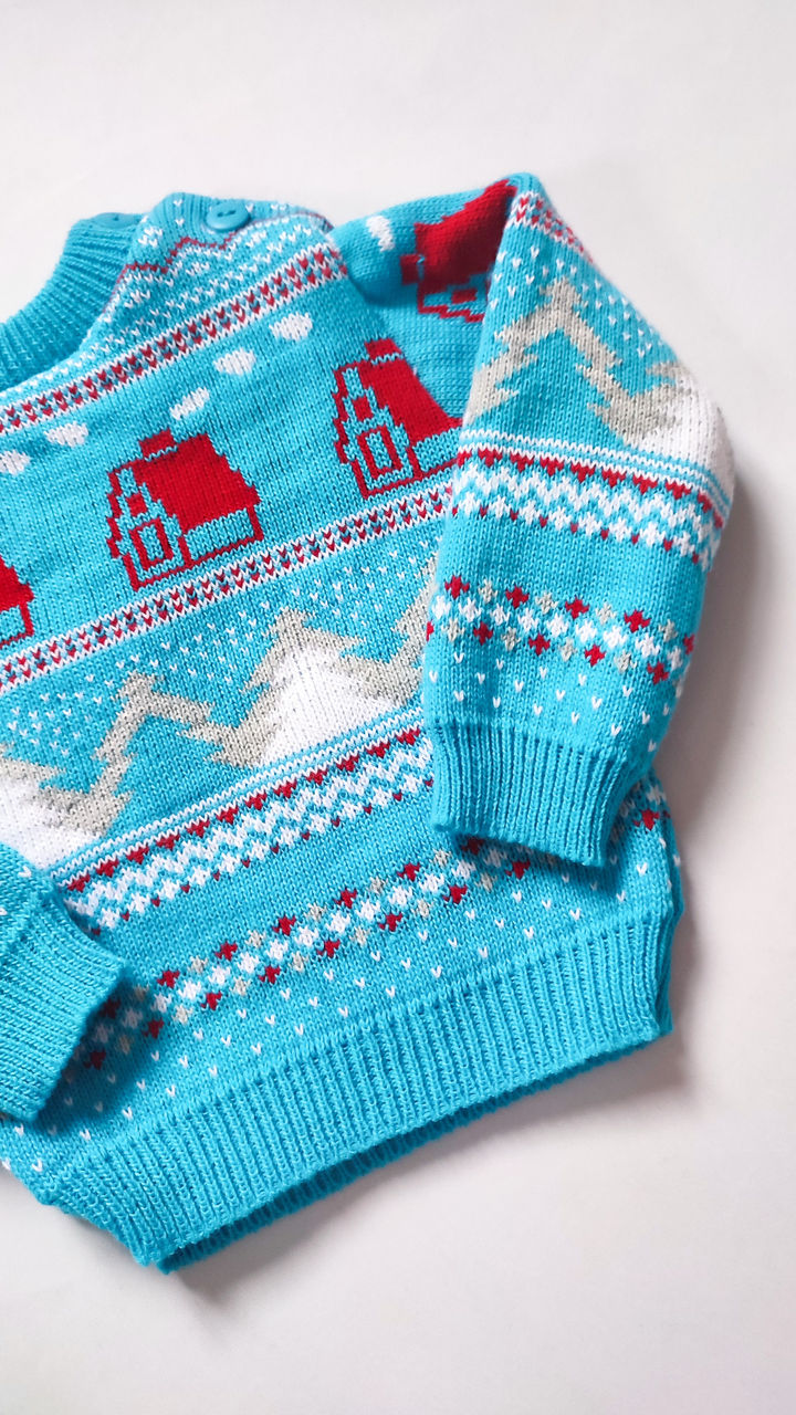 Blue Christmas jumper with red houses and snow covered Christmas tree pattern.
