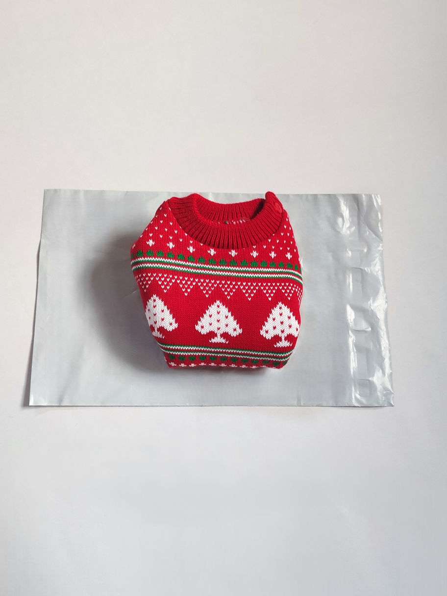 A folded red jumper with a festive winter design featuring, white trees, and decorative patterns, on grey parcel bag.