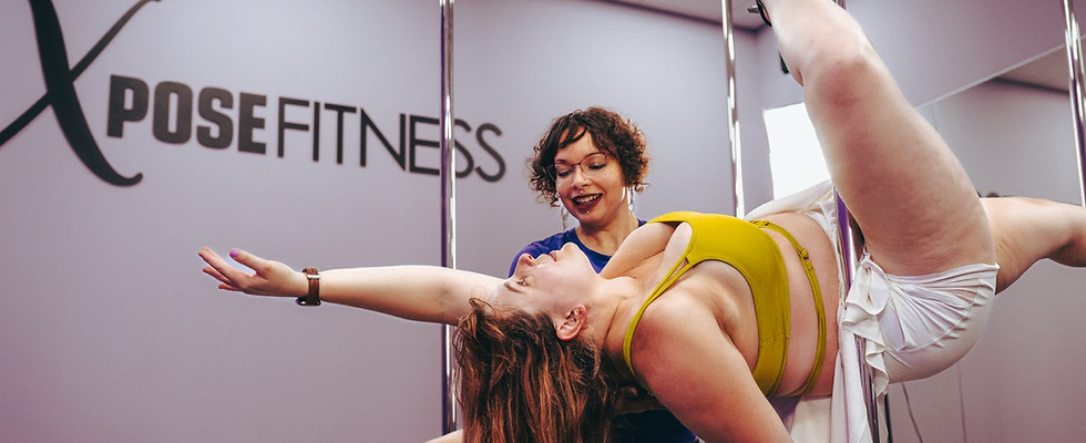 An instructor spotting a pole dance student at Xpose Fitness