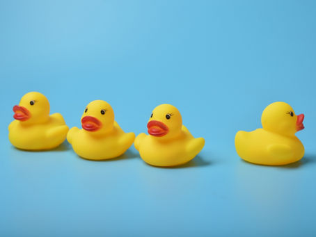 Four yellow rubber ducks on a light blue background. Three face right; one faces left. Ducks have orange beaks, creating a playful mood.