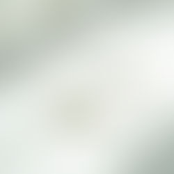 Gold chain bracelet with a green gemstone on a white surface, softly lit by sunlight. Minimalist and elegant design.