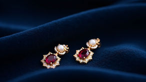 Gold earrings with red ruby gemstones and pearls on dark blue velvet fabric, creating an elegant and luxurious mood.