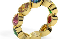 Gold ring with colorful teardrop gemstones arranged in a circle on a white background. Engraved initials "JM" inside.