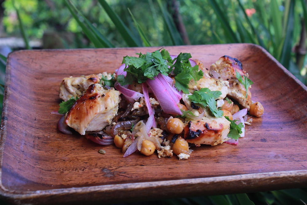 Wooden plate with baked chicken, chickpeas, onions and cilantro