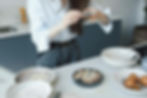 Person in a kitchen takes a photo of a baked dessert with a smartphone. Ingredients, bowls, and pears are on the countertop. Casual setting.