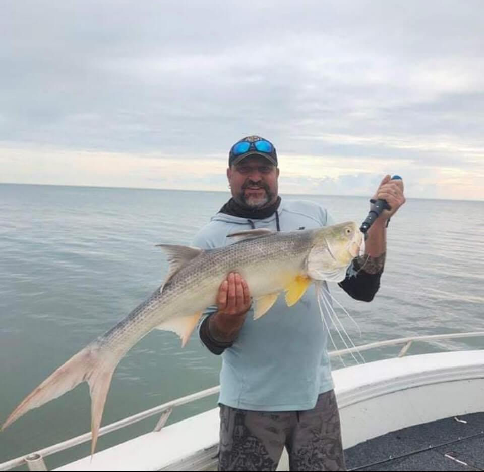 Travis smiling on deck with a sleek threadfin salmon, caught in calm coastal waters