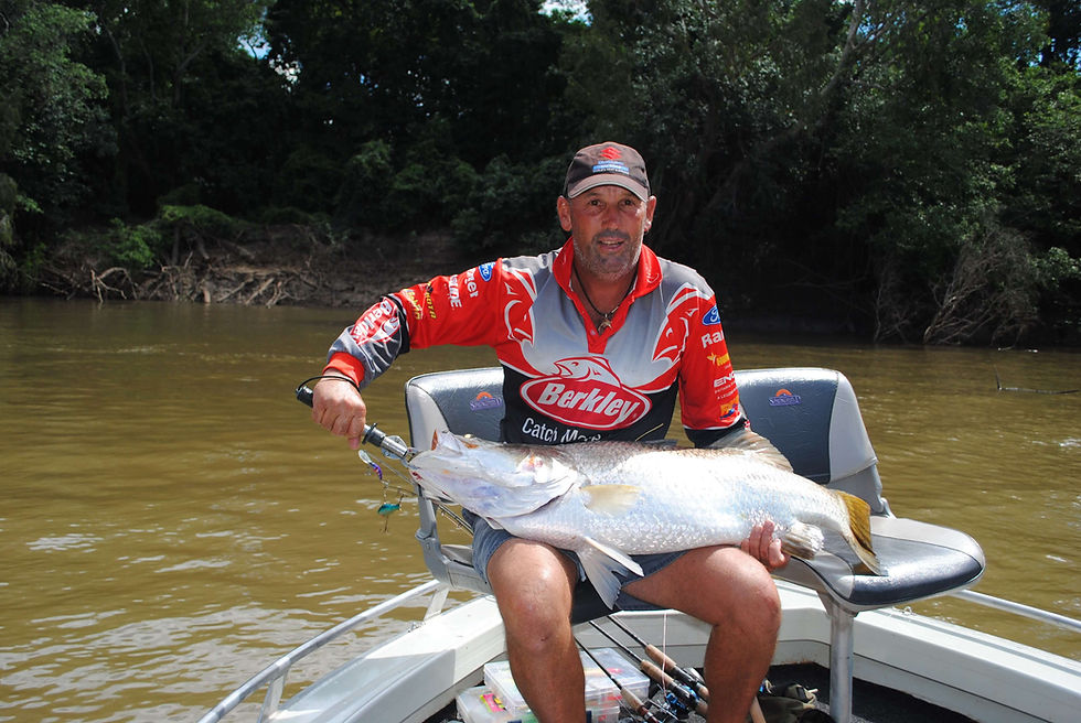 Man wearing a red Berkley shirt sitting in a boat, proudly holding a massive silver barramundi across his lap.